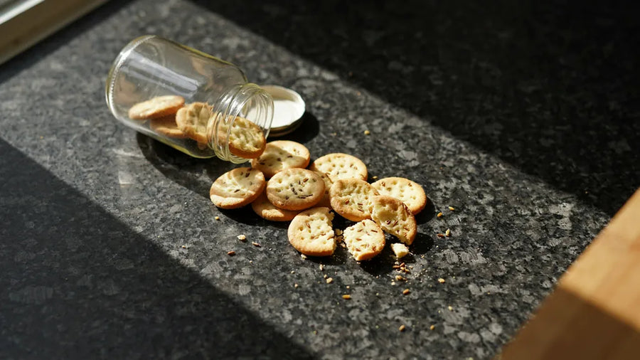 Flaky atta mathris with ajwain and fork marks spilling from a jar, made with CressPure Sharbati atta